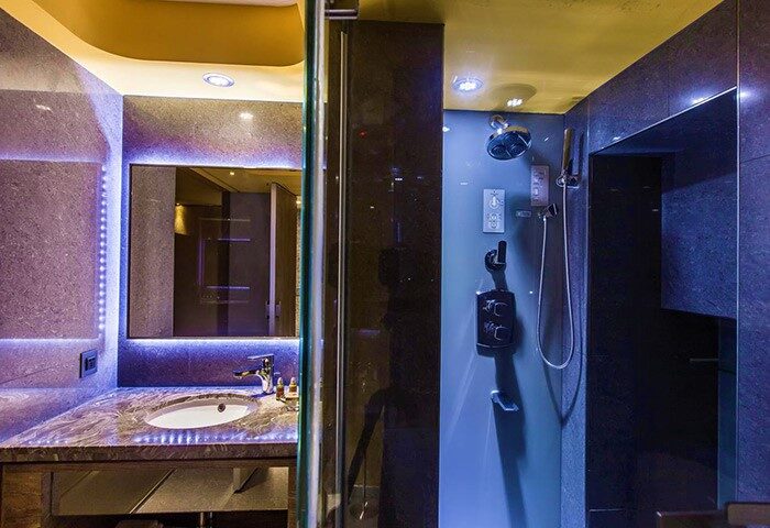Inhouse Hotel's gay-friendly bathroom. Modern design with a sink, mirror with LED lights, and a shower with dark tiles. A luxurious hotel experience.