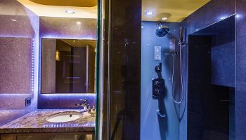 Inhouse Hotel's gay-friendly bathroom. Modern design with a sink, mirror with LED lights, and a shower with dark tiles. A luxurious hotel experience.