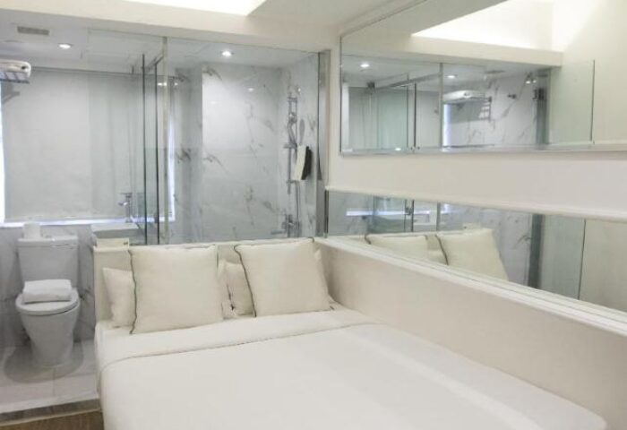 Mini Hotel Central gay-friendly room. Modern design with bed, pillows, and adjacent bathroom with glass shower. Mirrors enhance the space.