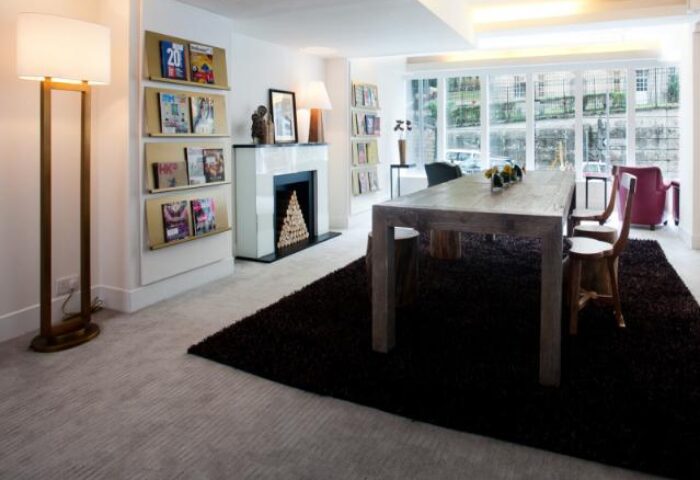 Central mini hotel's interior. Dining area with table, chairs, fireplace, magazines. Gay-friendly hotel design for gay men travel advice.