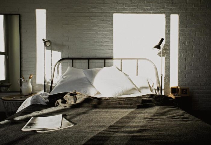 Room007 Chueca Hostel bedroom. Gay-friendly hotel room with bed, white brick wall, and sunlight. Ideal for gay men travel in Madrid.