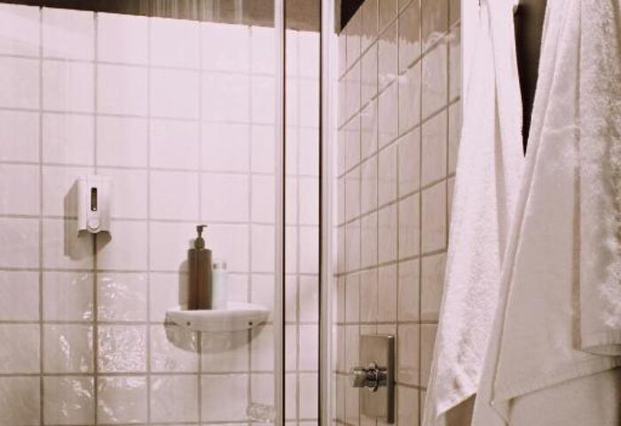 Shower at room007 Chueca Hostel, a gay-friendly hotel. Rainfall showerhead, white tiled walls, towels. Bathroom interior. Madrid travel.