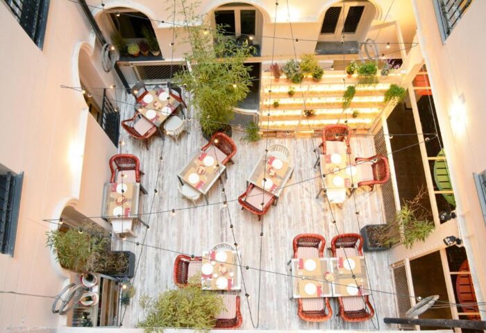 Room007 Chueca Hostel's gay-friendly courtyard. Aerial view of tables, chairs, plants, and string lights. A welcoming space in Madrid.