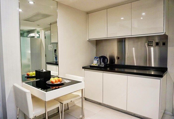 The Figo gay-friendly hotel room: kitchenette with white cabinets, black countertop, stainless steel backsplash, dining table, and chairs.