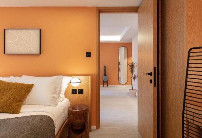 The Figo gay-friendly hotel room. Stylish interior with orange walls, wooden accents, bed, and a view into another room. Modern design.