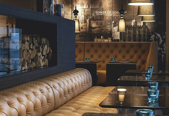 Motel One London Tower Hill interior. Stylish gay-friendly hotel lounge with leather seating, Tower of London mural, and modern lighting.