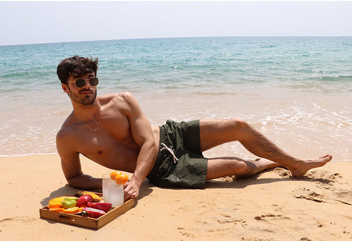 Gay-friendly Phuket beach resort: Man relaxing on sand with fruit tray. Renaissance Hotel offers spa, sun, and sea for gay travelers.
