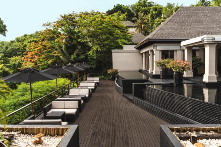 The Pavilions Phuket, a gay-friendly resort. Outdoor lounge area with umbrellas and seating. Tropical greenery surrounds the luxury resort.