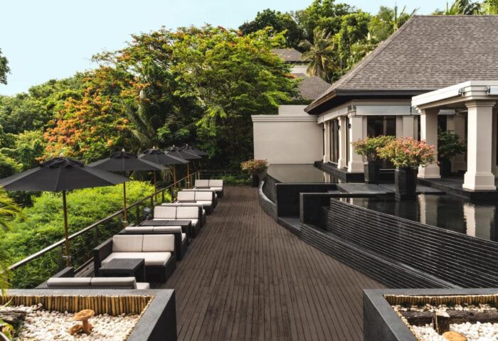 The Pavilions Phuket, a gay-friendly resort. Outdoor lounge area with umbrellas and seating. Tropical greenery surrounds the luxury resort.
