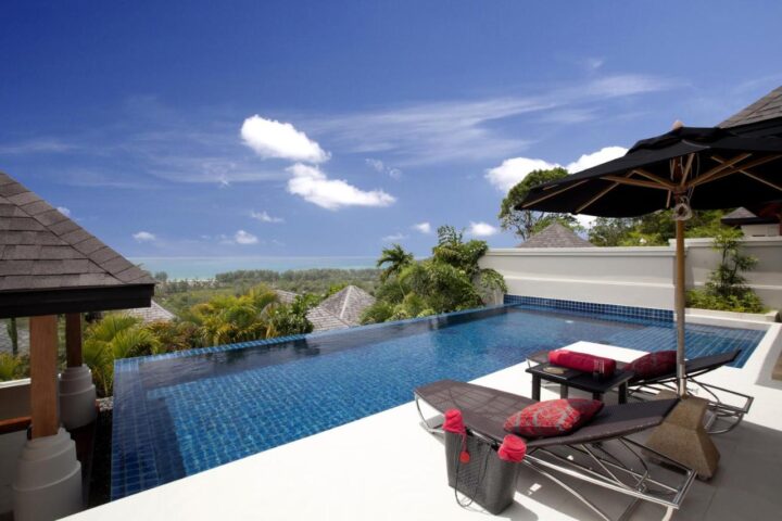 The Pavilions Phuket gay-friendly resort. Pool view with lounge chairs and umbrella. Tropical landscape with blue sky. Phuket, Thailand.