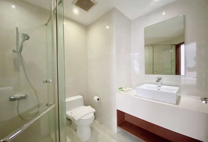Bathroom at The Luxe Hotel, a gay-friendly hotel in Ho Chi Minh City. Features a shower, toilet, and sink with mirror. Modern design.