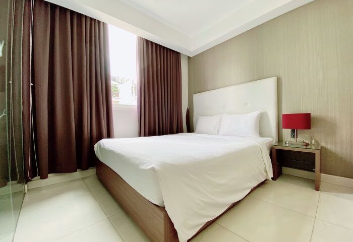 The Luxe Hotel room in Ho Chi Minh. Modern bedroom with white linens, brown curtains, and a red lamp. Gay-friendly hotel in Vietnam.