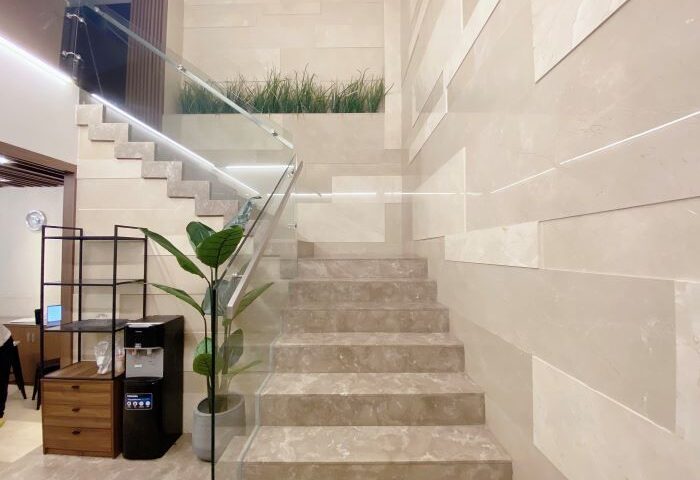 Staircase at The Luxe Hotel, a gay-friendly hotel in Ho Chi Minh City. Modern design with glass railings and marble steps, plants add a touch of nature.