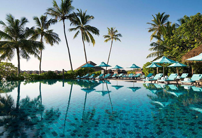 Anantara Veli Maldives Resort beachfront pool. Gay-friendly hotel with turquoise umbrellas, sun loungers, and palm trees reflected in the pool.