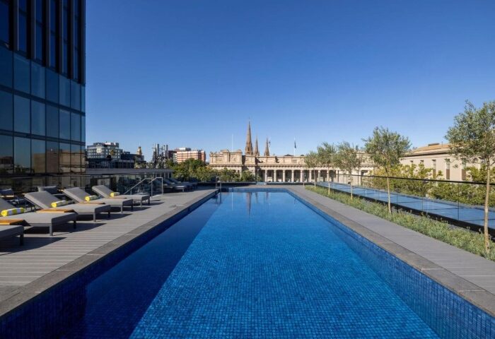 Le Meridien Melbourne gay-hotel rooftop pool. Loungers, city view, and blue sky. Perfect for gay travelers seeking luxury in Melbourne.