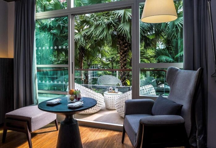Pullman Bangkok King Power hotel room with garden view. Gay-friendly hotel with balcony, table, chairs, and tropical foliage.