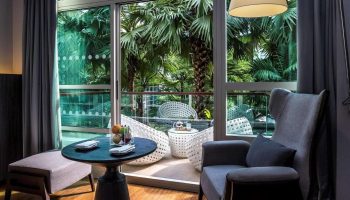 Pullman Bangkok King Power hotel room with garden view. Gay-friendly hotel with balcony, table, chairs, and tropical foliage.