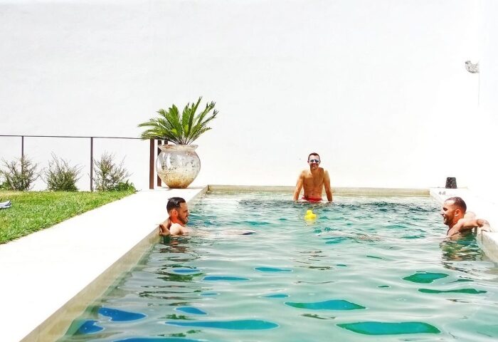 Gay men relax in the pool at The Late Birds Lisbon, a gay urban resort. A yellow duck floats in the water. Gay hotspot hotel in Lisbon.