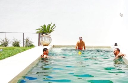 Gay men relax in the pool at The Late Birds Lisbon, a gay urban resort. A yellow duck floats in the water. Gay hotspot hotel in Lisbon.