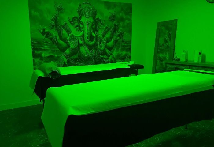 Gay massage in Gran Canaria. Two massage tables in a room with a green light. A tapestry with an elephant god is on the wall.