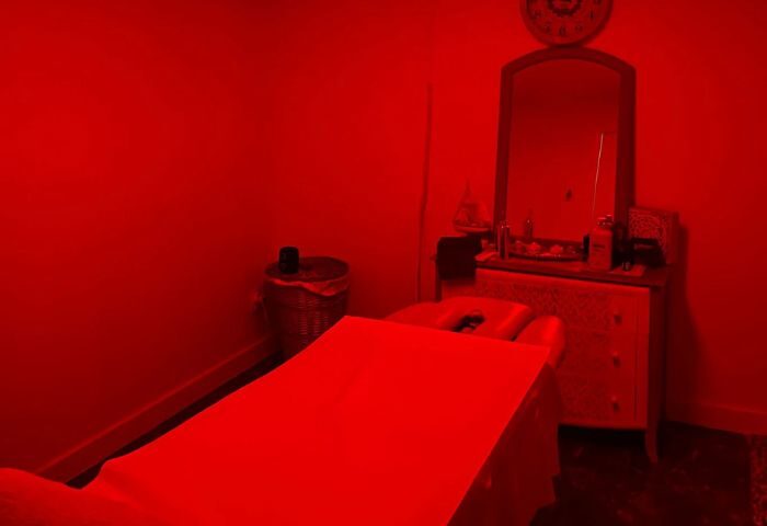 Red-lit room for a gay massage in Gran Canaria. Massage table, dresser with mirror, and a waste bin are visible. Relaxing gay travel experience.