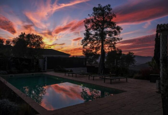 Casa Brisa Boutique Guest House sunset view. Gay-owned guesthouse with pool and lounge chairs. Scenic sky reflecting in the water.