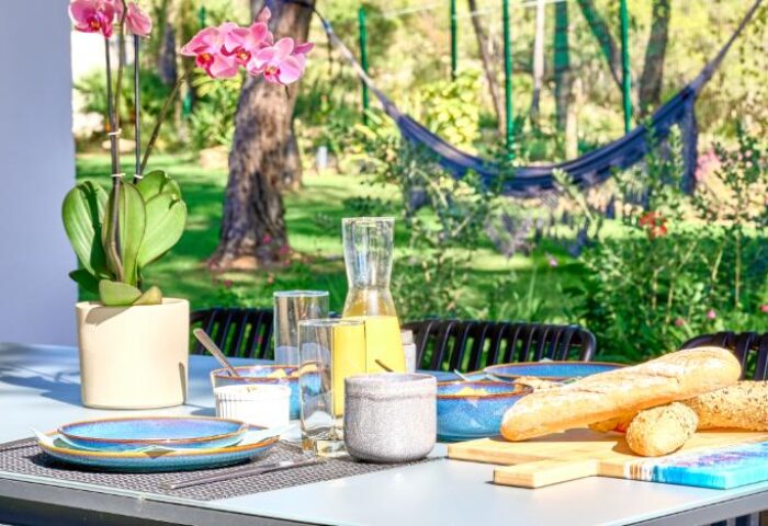 Casa Brisa Boutique Guest House's outdoor dining area. Table setting, bread, juice, and orchid. Gay-owned guesthouse with garden view.