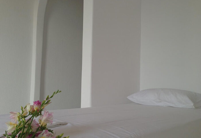 Minimalist room at M for Mykonos, gay-popular hotel in Mykonos Town near gay bars. White walls, bed, pillow, flowers. LGBTQ+ travel.