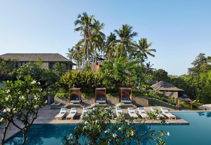 Nirjhara Bali jungle hotel pool view. Gay-popular resort with sunbeds, palm trees, and lush greenery. Perfect for gay men's travel in Bali.