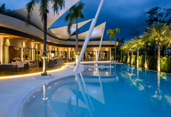 The Pavilions Phuket gay resort. Luxury pool at dusk. Upscale dining and lounge areas. Palm trees. Gay travel in Phuket, Thailand.