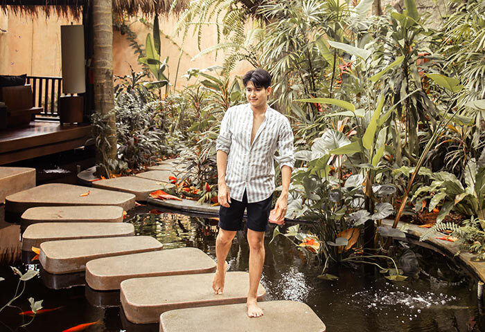 Gay wellness beach resort in Koh Phangan. Man walking barefoot on stepping stones over a pond at Anantara Rasananda Koh Phangan Villas.