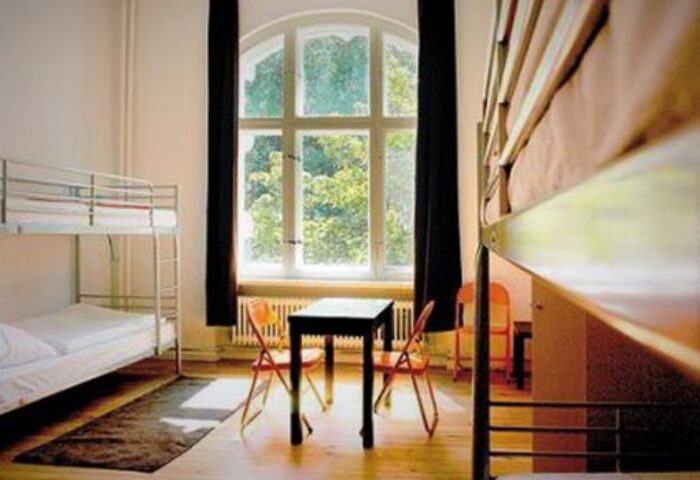 Dorm room at gay youth hostel in Berlin. Bunk beds, table, chairs, and large window. Ideal for young gay solo travelers near a gay home.