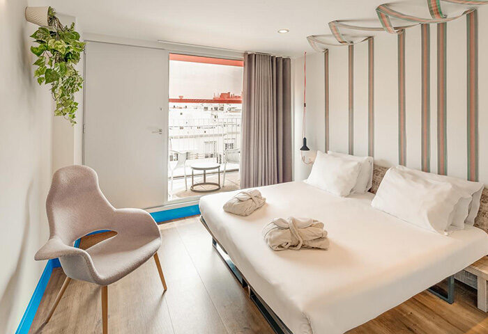 Generator Barcelona private room with balcony. Gay hostel bed & bath. Modern design, light wood floors, white linens, and city view.