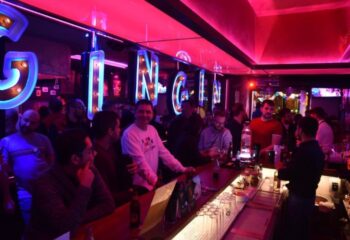 GinGin Gay Bar in Barcelona. Interior view of the bar with patrons, illuminated by pink and blue lights. Gay travel advice.