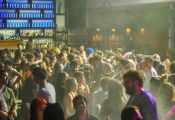 Glamorize Roma: A crowded gay bar in Rome, Italy. People are dancing and socializing. Bottle-lined bar in the background. Nightlife scene.