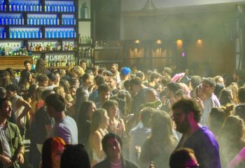 Glamorize Roma: A crowded gay bar in Rome, Italy. People are dancing and socializing. Bottle-lined bar in the background. Nightlife scene.
