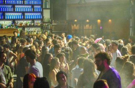 Glamorize Roma: A crowded gay bar in Rome, Italy. People are dancing and socializing. Bottle-lined bar in the background. Nightlife scene.