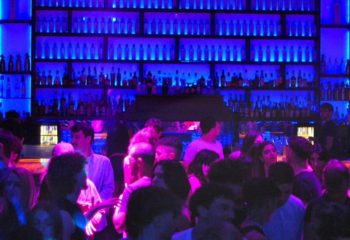Glamorize Roma: A lively gay bar scene in Rome, Italy. Crowd of people enjoying drinks under blue lighting. Gay travel advice.