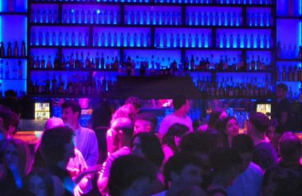 Glamorize Roma: A lively gay bar scene in Rome, Italy. Crowd of people enjoying drinks under blue lighting. Gay travel advice.