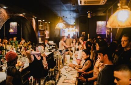 Good Judy Bar, New York. Bartender pouring drinks for a crowded bar. Gay bar scene with people enjoying drinks. Queer nightlife.