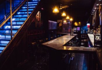 Good Judy Bar for queers in New York. Interior view of the bar with blue-lit stairs, bar counter, and seating. A gay travel destination.