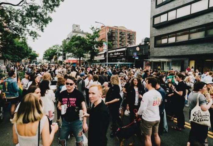 Good Judy Bar, a queer bar in New York, hosts a crowded outdoor event. Gay men and others gather on the street.