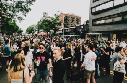 Good Judy Bar, a queer bar in New York, hosts a crowded outdoor event. Gay men and others gather on the street.