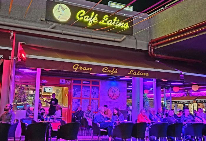 Gran Cafe Latino gay bar in Gran Canaria. People sit outside under the awning at tables. Neon sign above.