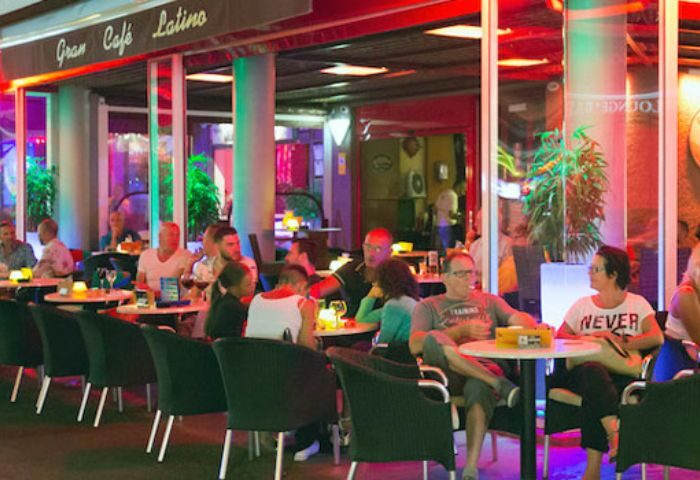 Gran Cafe Latino, a gay bar in Gran Canaria. People sit at tables outside, enjoying drinks in the vibrant, colorful atmosphere.