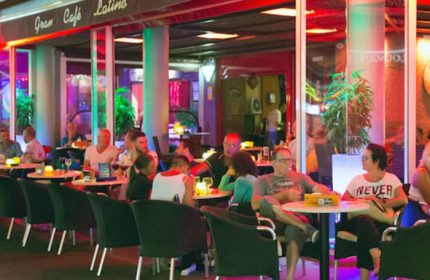Gran Cafe Latino, a gay bar in Gran Canaria. People sit at tables outside, enjoying drinks in the vibrant, colorful atmosphere.