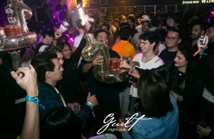 Guilt Night Club, a gay bar in Mexico. A crowd of people are gathered, some holding drinks on a unicorn-shaped tray. Nightlife scene.