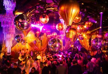 Guilt Night Club, a gay bar in Mexico. Disco balls and hot air balloon decorations hang above a crowded dance floor. Purple lighting.