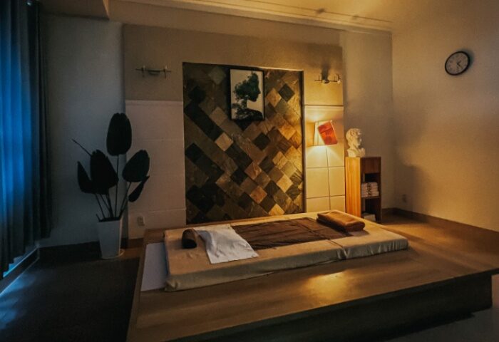 Guu Spa Ho Chi Minh: Massage bed in a warmly lit room with decorative wall, plant, and bust. Gay travel advice in Vietnam.