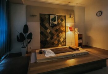 Guu Spa Ho Chi Minh: Massage bed in a warmly lit room with decorative wall, plant, and bust. Gay travel advice in Vietnam.